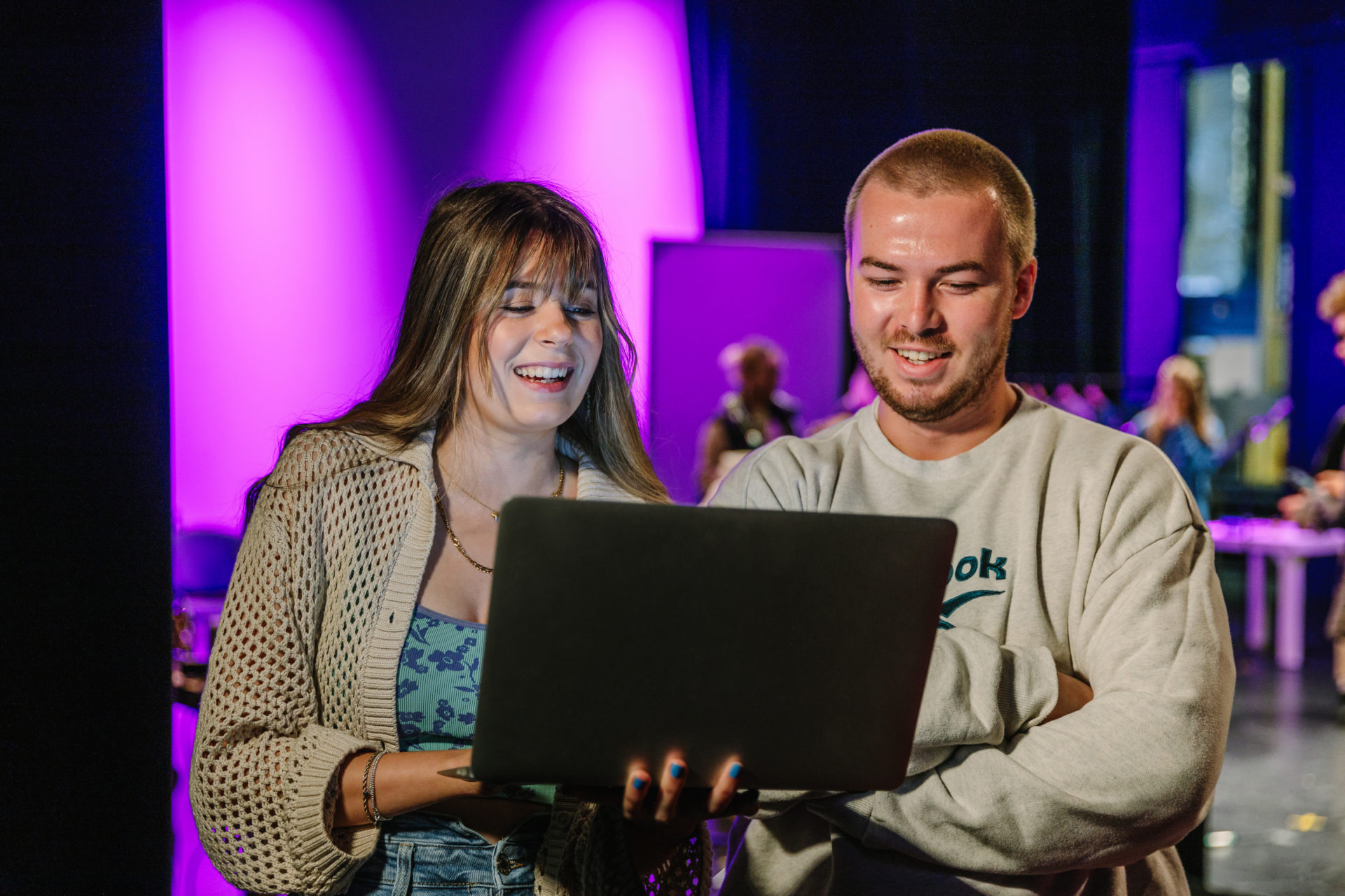 Bethan and Harry look at a laptop and smile in the theatre